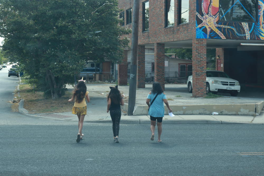 Three girls dart across busy Zarzamora at San Fernando, avoiding traffic.